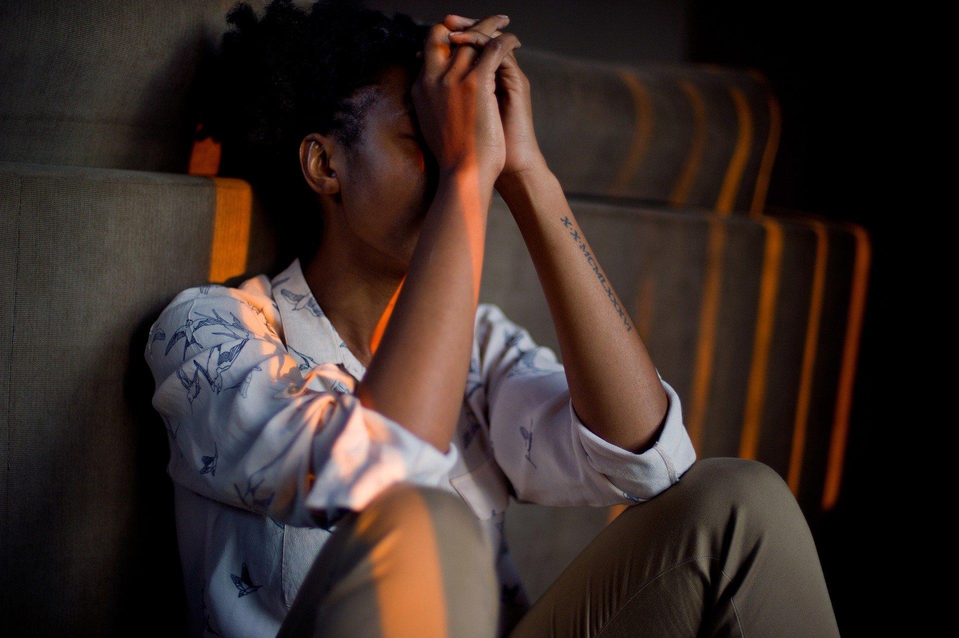 Black woman leaning against wall, hands to face, indicating stress