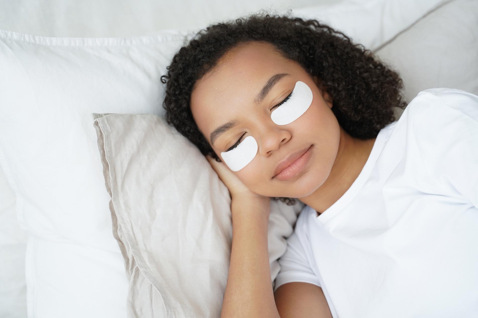 young biracial girl with under eye patches on face relax lying in bed morning skincare routine