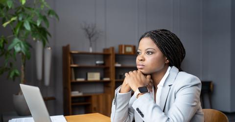 Young thoughtful african female employee looking out window at workplace and dreaming about vacation