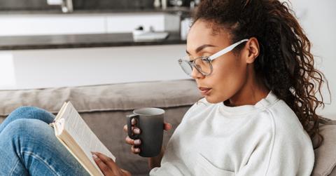 Image of smart african american girl reading book and drinking t