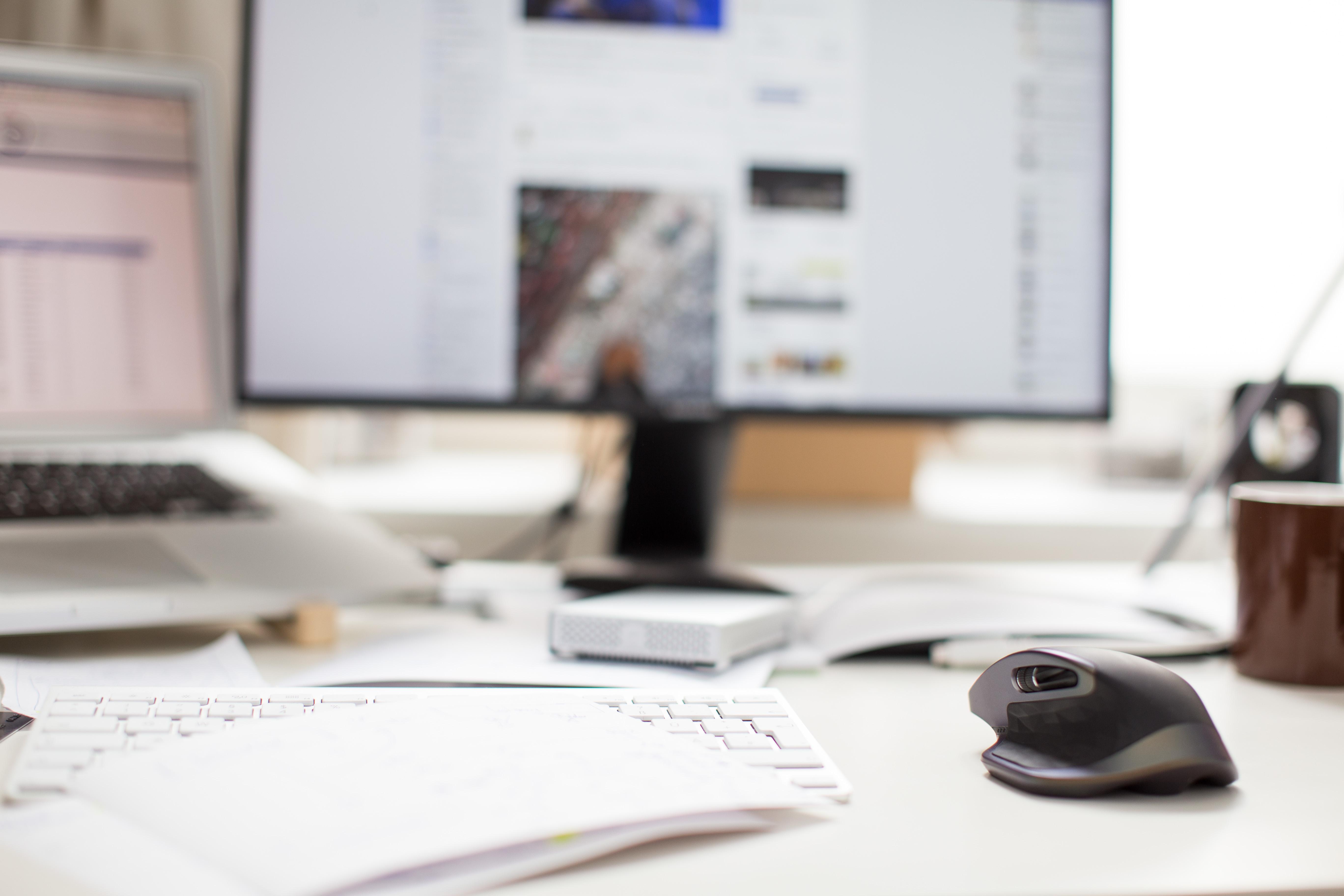 A slightly cluttered desk sits in the foreground with an out of focus monitor in the background.