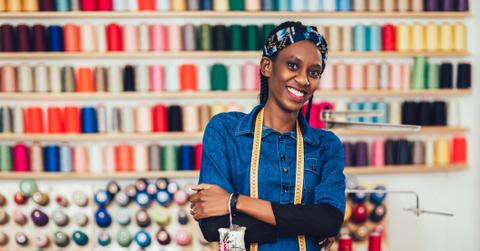 Portrait of happy african fashion designer woman in studio. Background of colorful sewing thread.