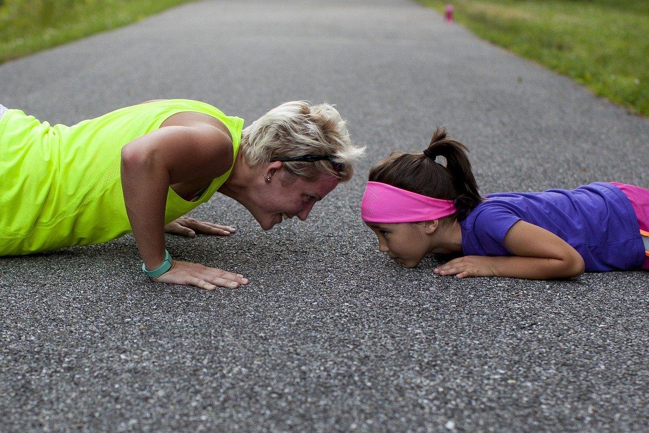 woman and child face to face doing pushups on a paved trail