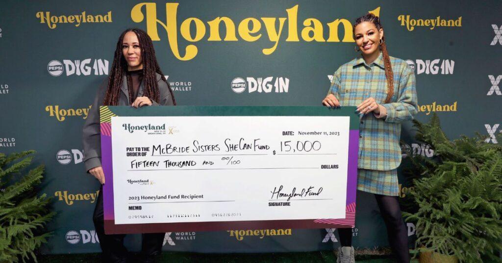 Robin McBride and Andréa McBride attend Honeyland Festival Day 1, holding a SHE CAN Fund donation check