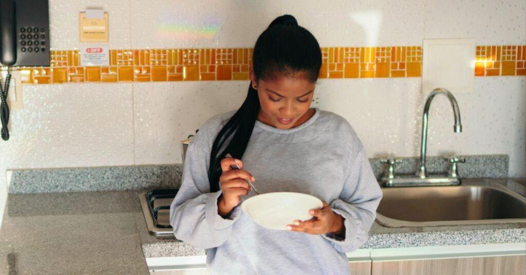 woman eating from bowl while standing in the kitchen