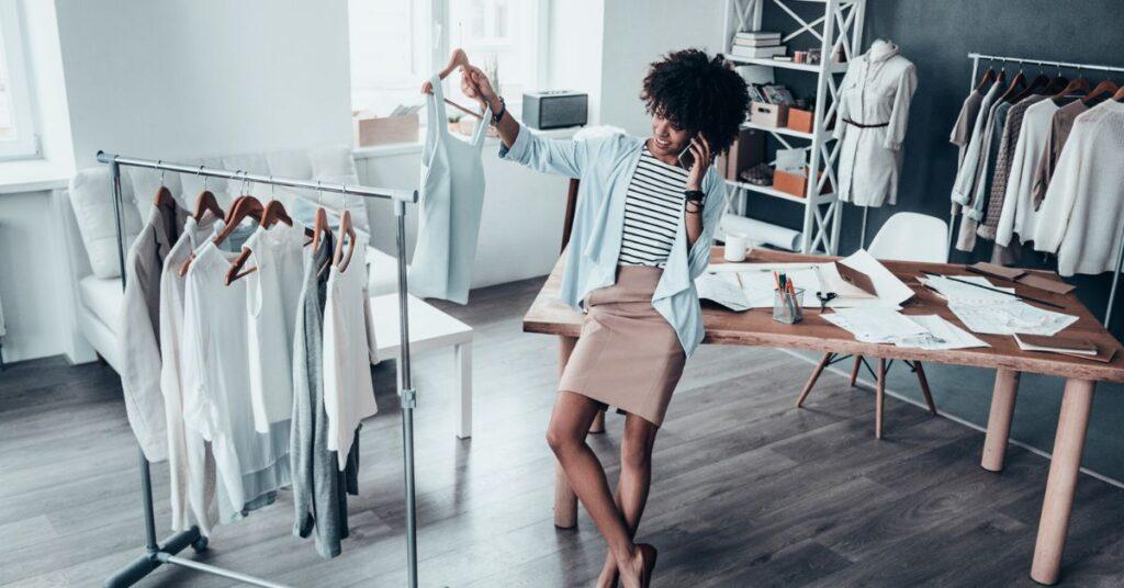 Black woman designer on phone looking at clothes in a design studio