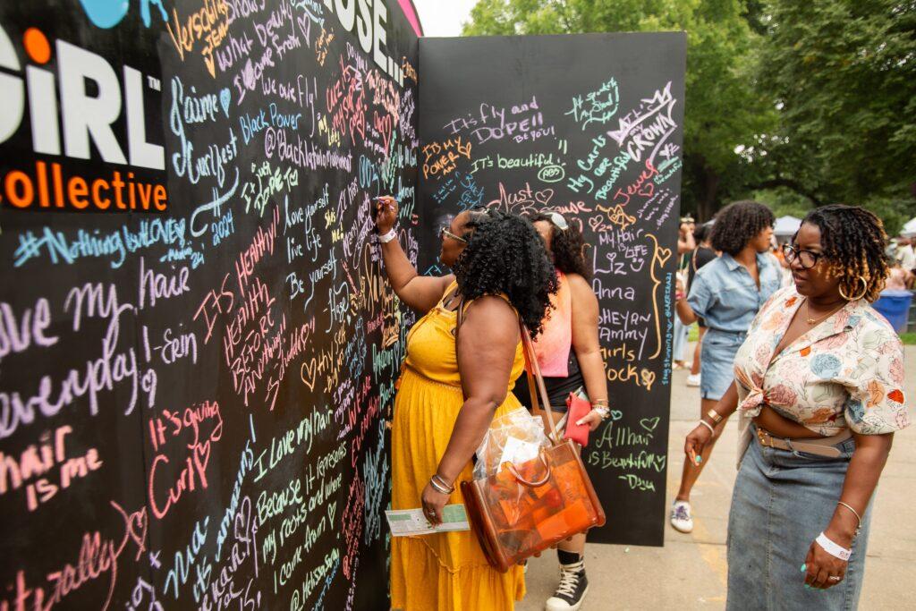 Event attendees express why they love their hair on the "I love my hair because..." chalkboard wall at CurlFest