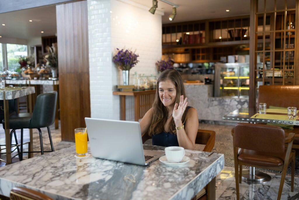 woman at coffee shop waving to laptop