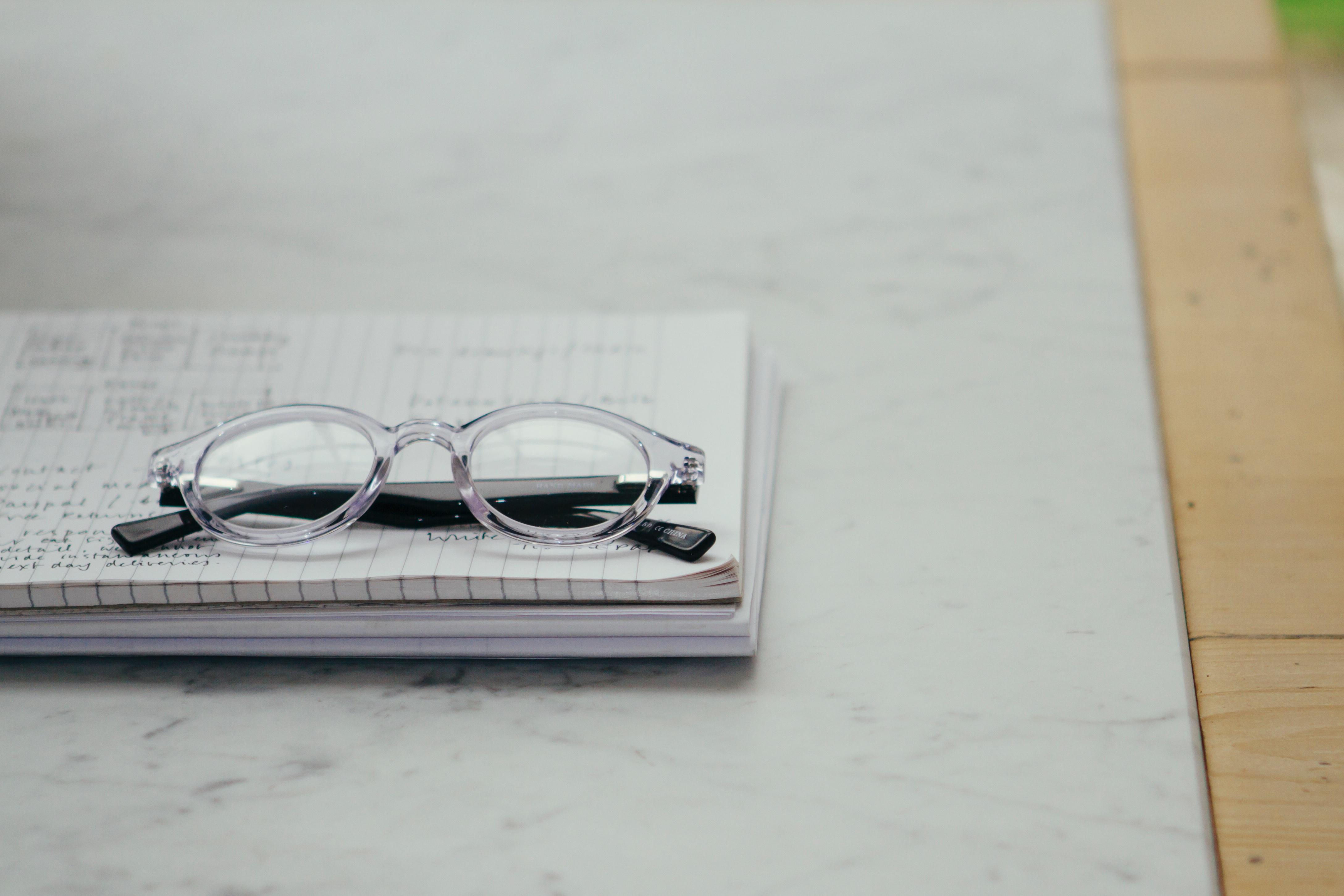 A pair of clear framed glasses sits upon a notebook.