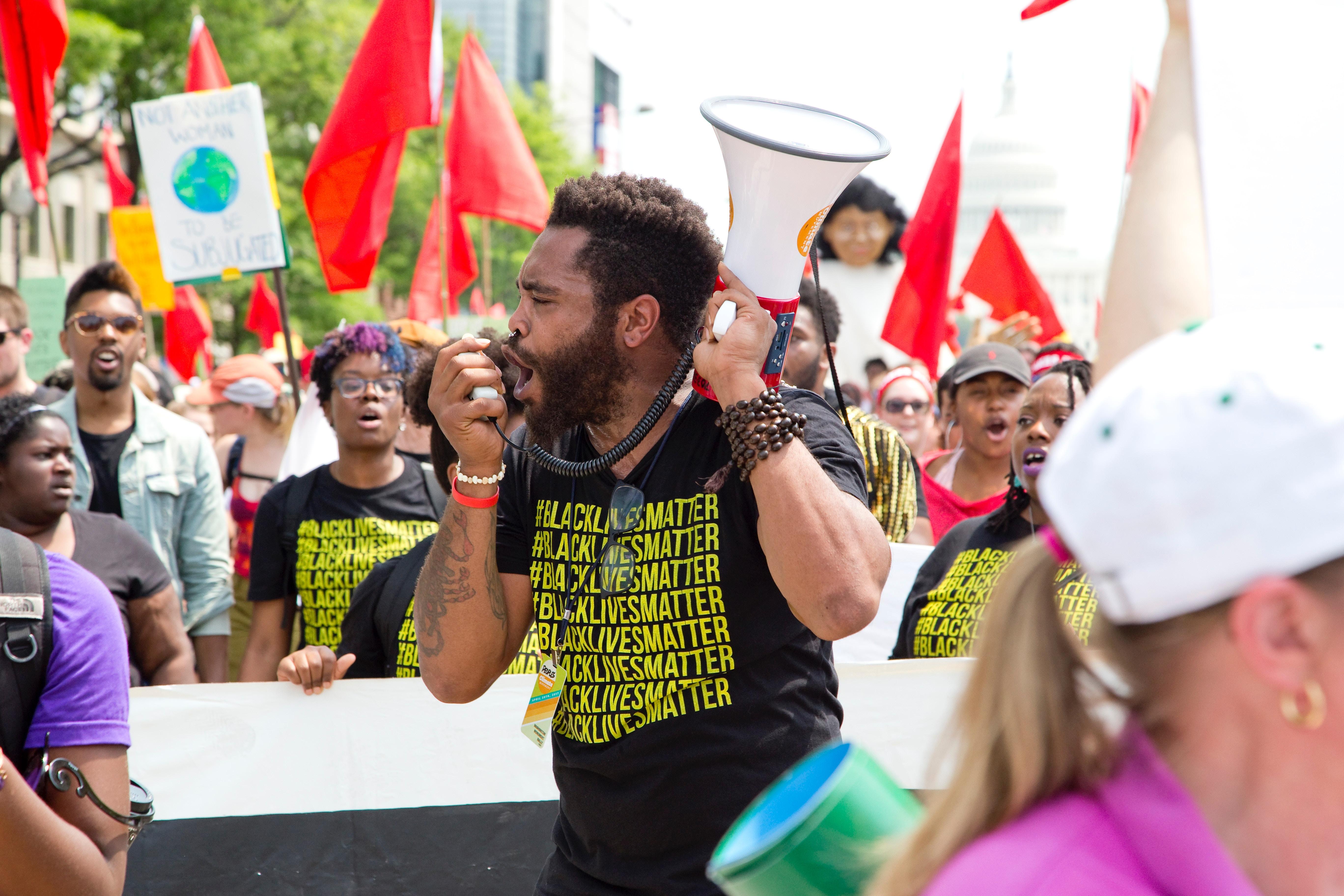 A man with a megaphone wearing a black lives matter t-shirt at a protest.