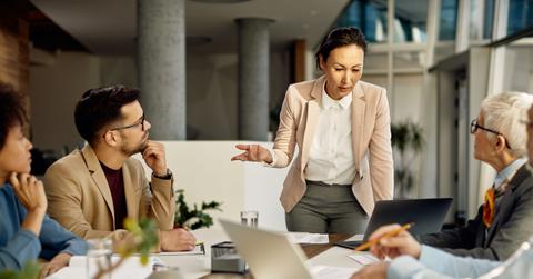 Asian female leader using laptop and communicating with her business team during meeting in the office.