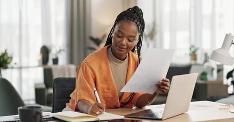 Black woman in home office, documents and laptop for research in remote work, ideas and thinking. Happy girl at desk with computer, writing notes and online search in house for freelance networking.