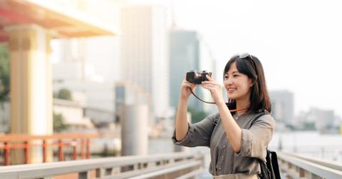 Young Asian woman backpack traveler using a camera in express boat pier on Chao Phraya River in Bangkok.