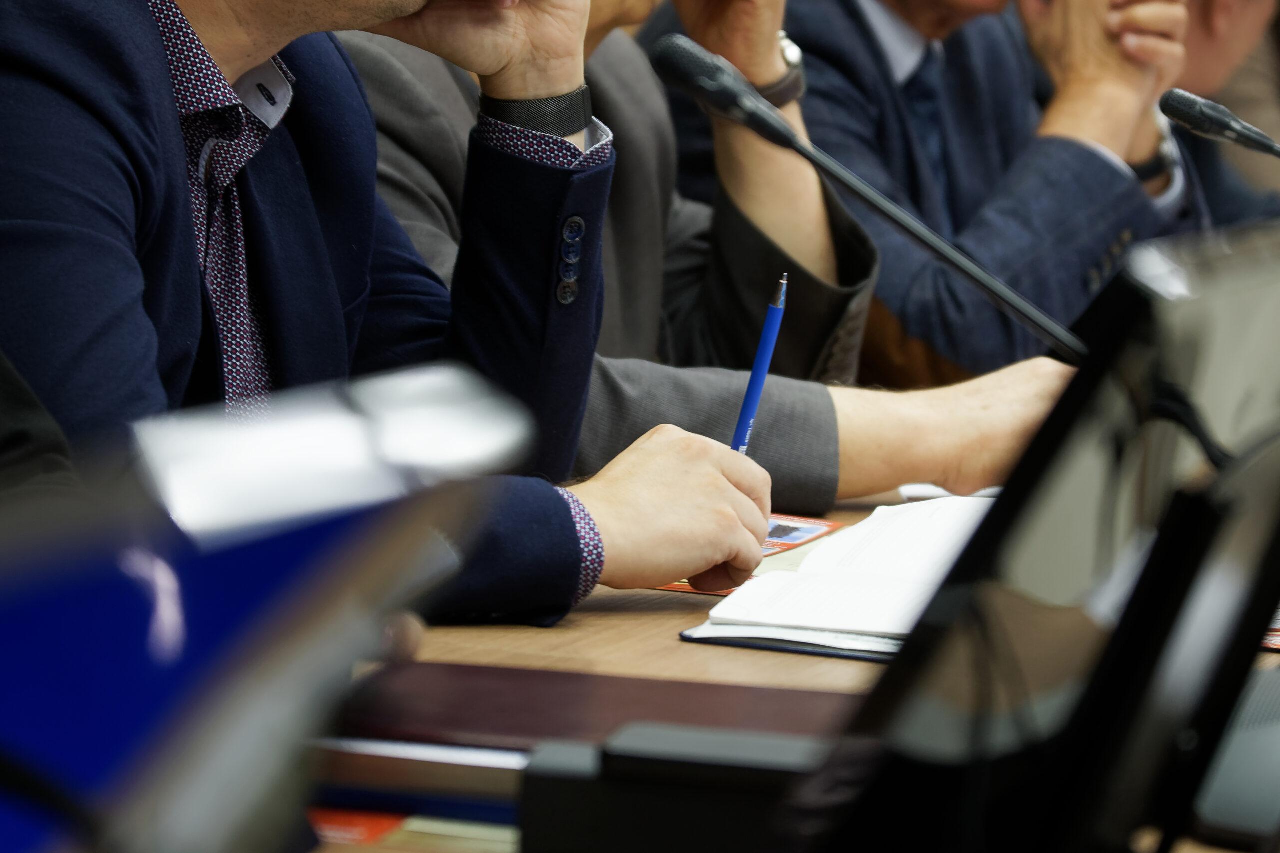 Participants in a business meeting with notebooks, pens, watches