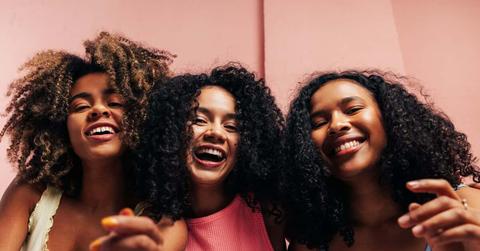 Three happy girlfriends with curly hair laughing together and looking at camera