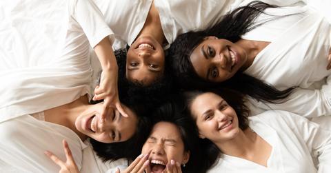 Five happy diverse young girls lying on bed, top view