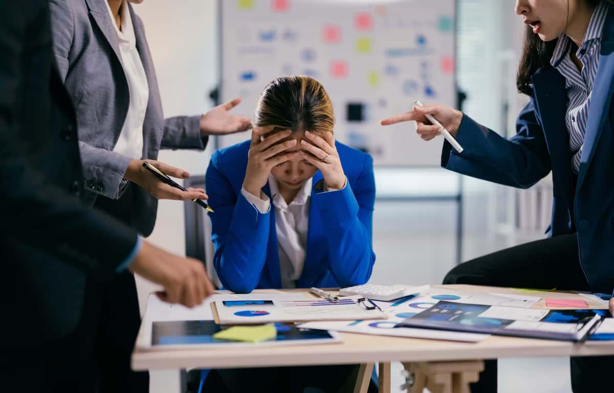Businesswoman is feeling stressed while her coworkers are being aggressive and blaming her for something during a business meeting