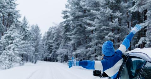 Rear view of adult woman in car over snowy forest on winter roadtrip.