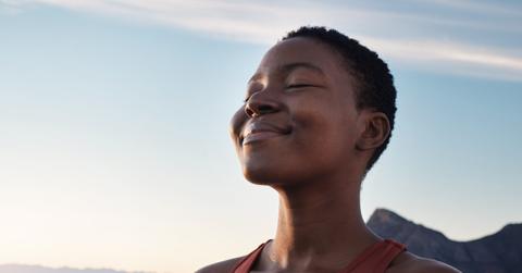 Fitness, calm and breathing of black woman outdoor in nature, mountains and blue sky background for yoga wellness, meditation and zen energy. Face of girl breathing for peace, freedom and mindfulness