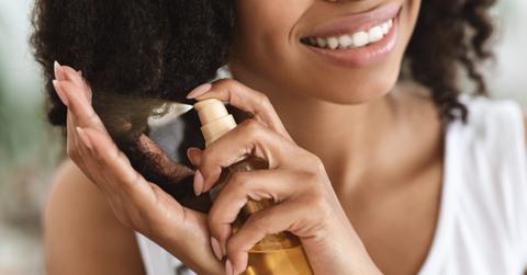Split Ends Treatment. Smiling Black Woman Spraying Essential Oil On Curly Hair
