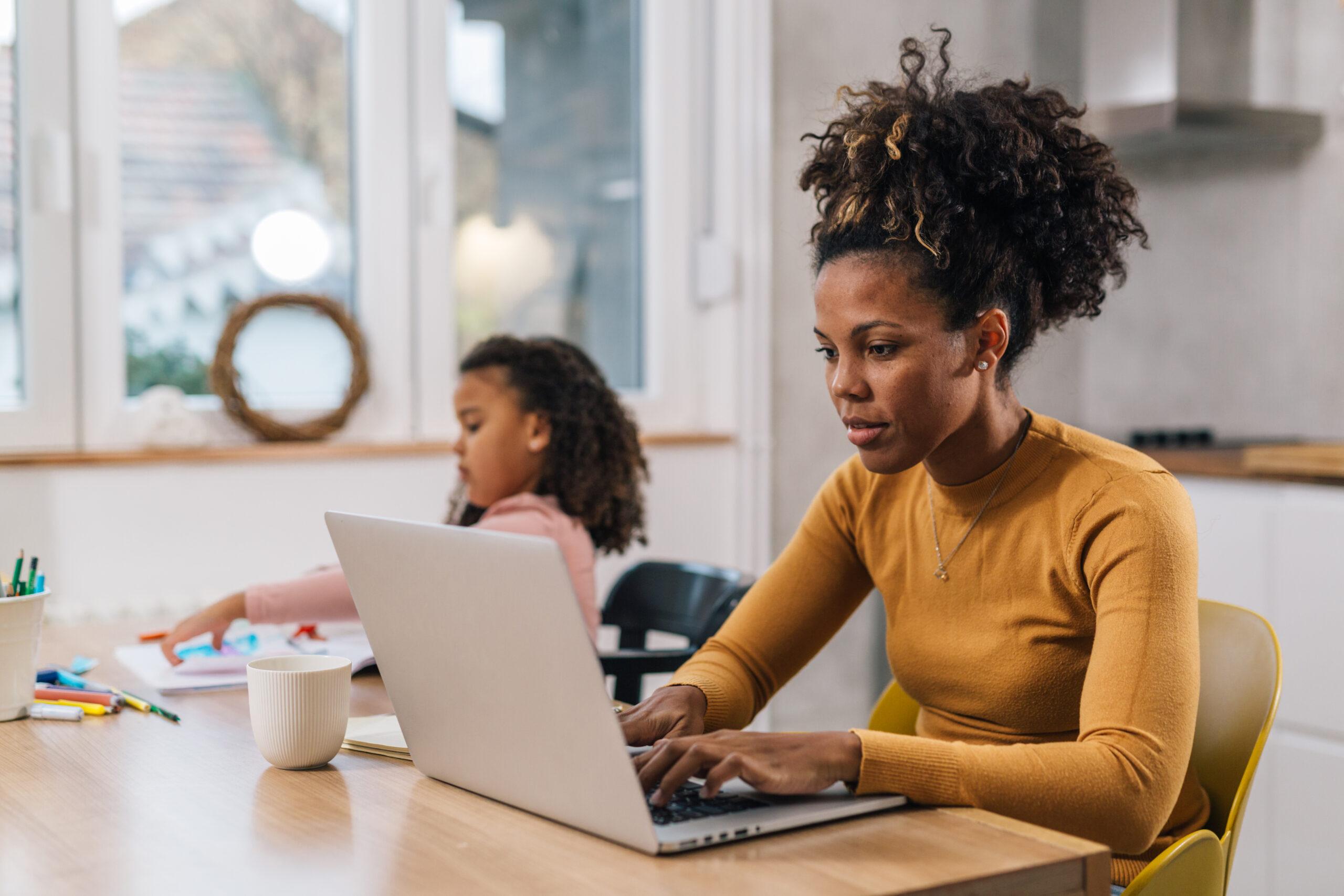 Mom is working from home with her daughter sitting next to her