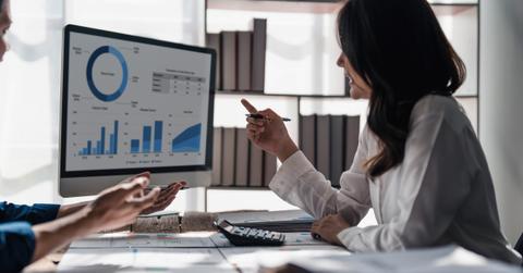 Two business people talk project strategy at office meeting room. Businessman discuss project planning with colleague at modern workplace while having conversation and advice on financial data report.