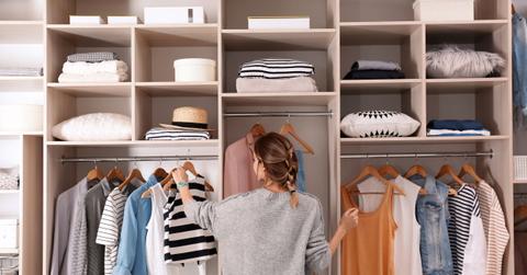 Woman choosing outfit from large wardrobe closet with stylish cl