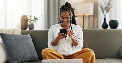 Happy, black woman and credit card with phone on sofa for online shopping, payment code and fintech at home. Mobile banking, finance and password to upgrade subscription, ecommerce and money savings