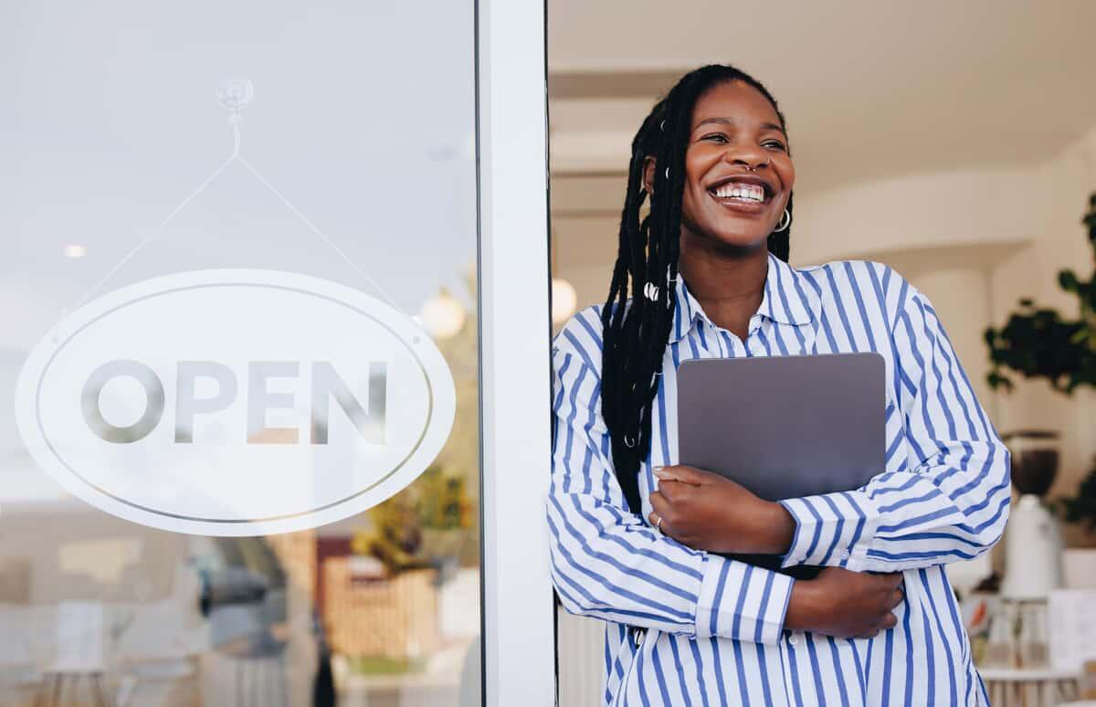 Successful small business owner standing next to an open sign in her new cafe
