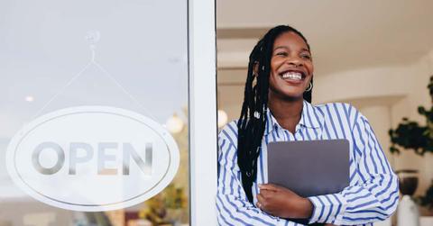 Successful small business owner standing next to an open sign in her new cafe