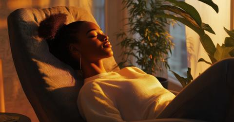 Peaceful smiling young Black woman resting in cozy soft armchair, breathing fresh air, enjoying being at comfortable home. Millennial girl reloading mind, practicing stress relief, mindfulness