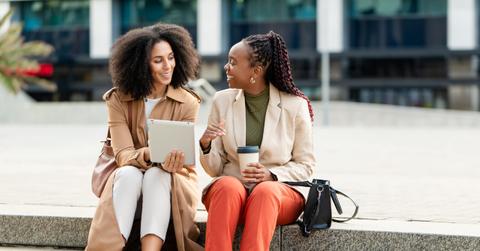 Two Black Businesswomen Discussing Ideas on a Tablet While Seated Outdoors