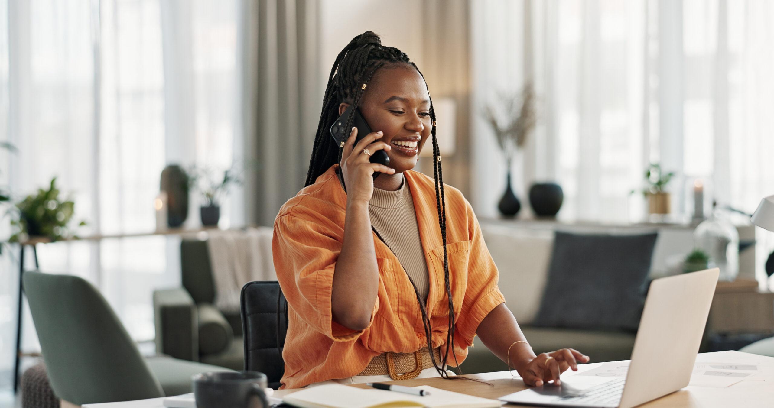 Black woman in home office, phone call and laptop for remote work, social media or content management. Happy girl at desk with computer, cellphone and online chat in house for freelance networking.