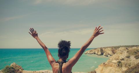 Black woman with open arms looking at the sea sitting on a cliff in Algarve, Portugal