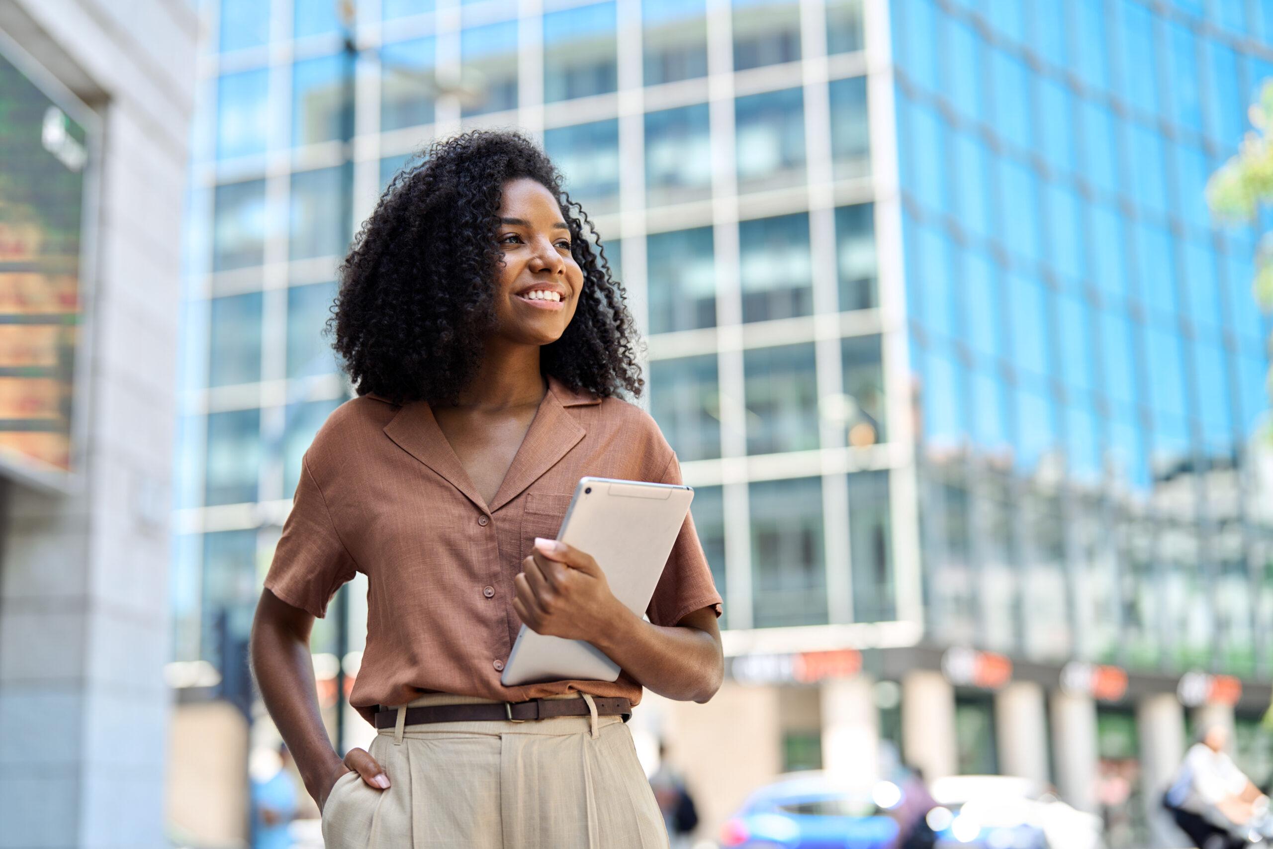 Happy young African American professional woman looking away standing in city.