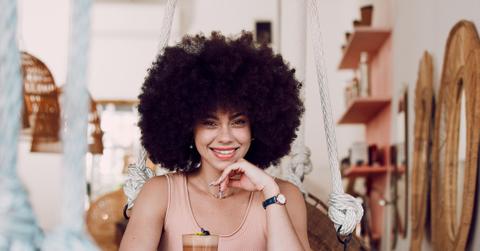 Black woman in coffee shop portrait with drink, relax with natural hair and smile, happy alone for self care date and pride with afro for self love. Happiness, African woman in cafe for coffee break.
