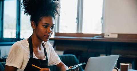 Portrait of a self-employed black woman barista at her coffee shop counter working on laptop. Confident entrepreneur managing finance bookkeeping in her own business.