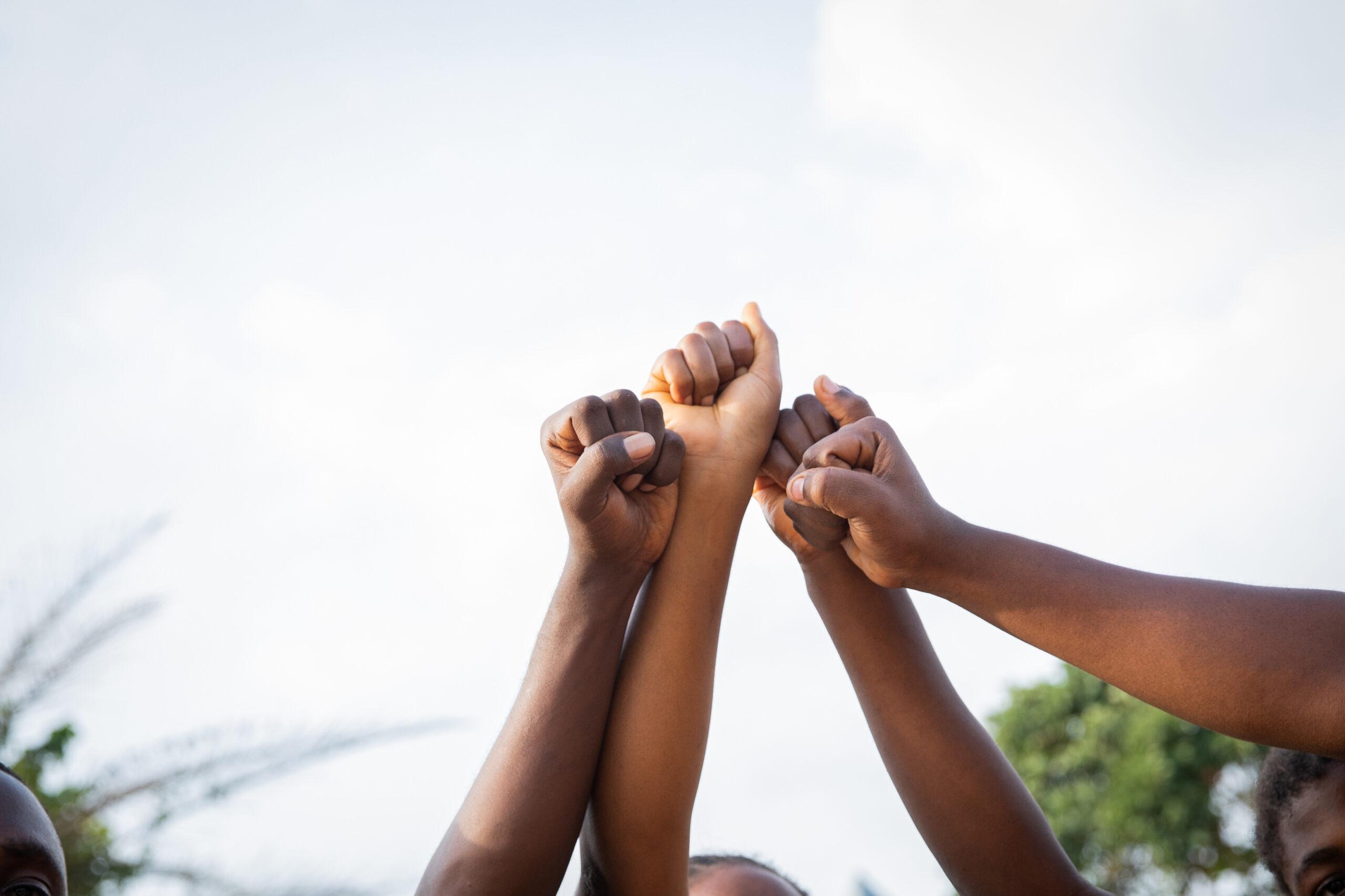 Four fists of African people united in sky, photo with copy space.