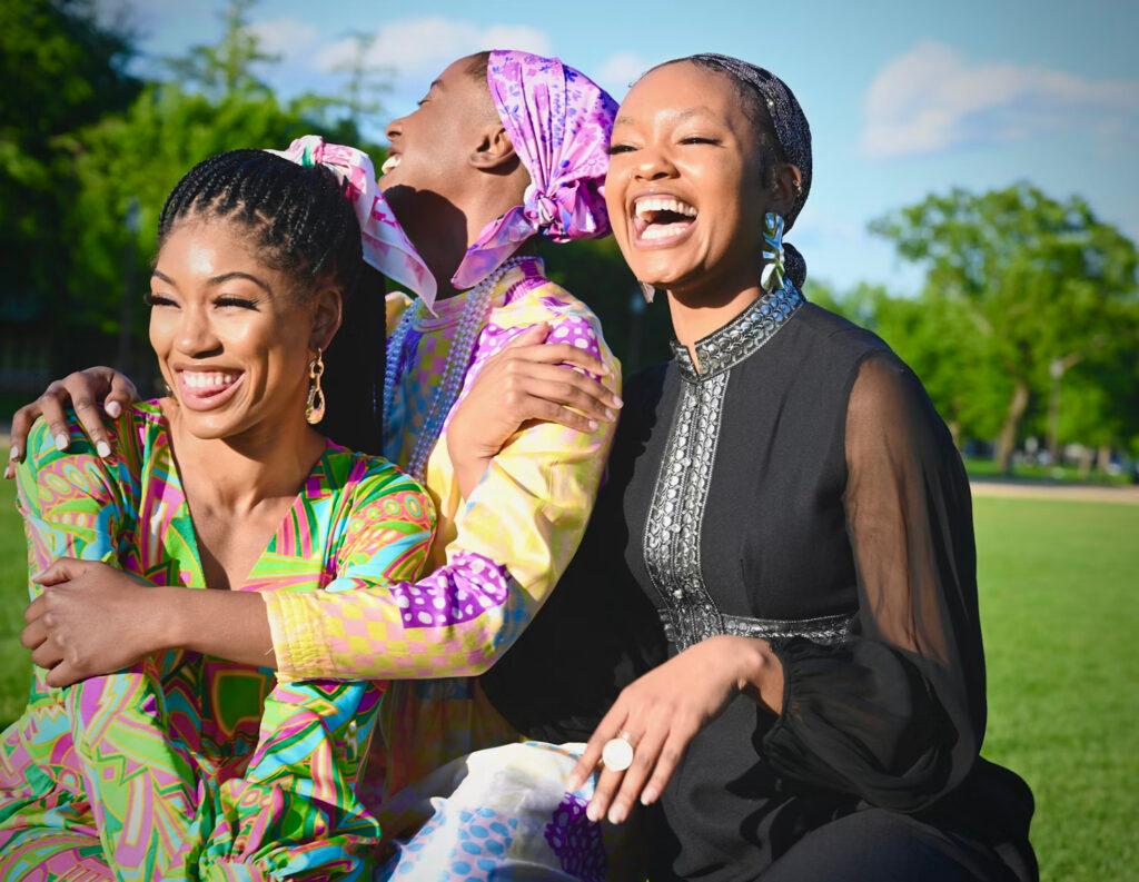 Three young Black women laugh together outdoors, illustrating the empowerment and joy found in female friendship and community.