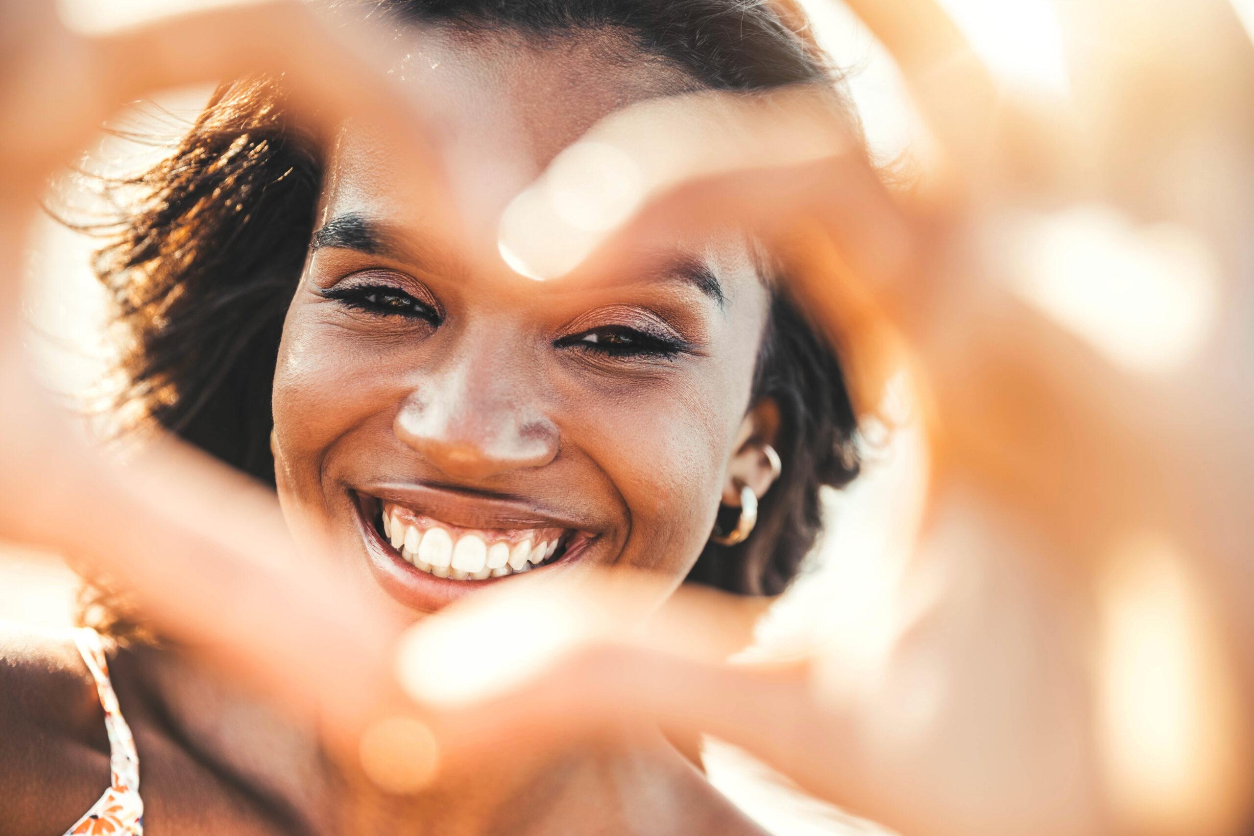 Beautiful young woman making heart shape with hands &#8211; Happy black woman smiling at camera outdoors &#8211; Health care and self love concept