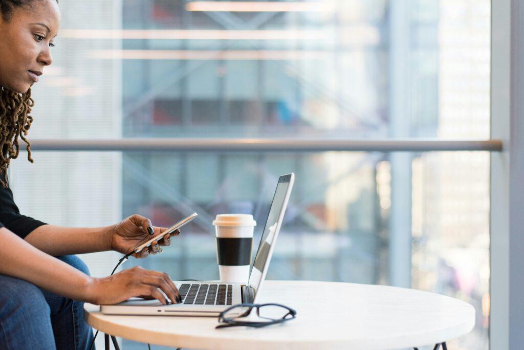 Professional woman multitasking on laptop and phone in a modern coworking space, managing her freelance business during Q4.