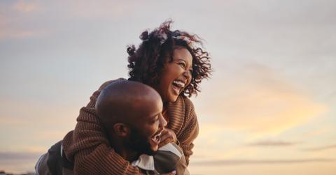 Black couple, travel and beach fun while laughing on sunset nature adventure and summer vacation or honeymoon with a piggy back ride. Comic, energy and black man and woman love on ocean holiday