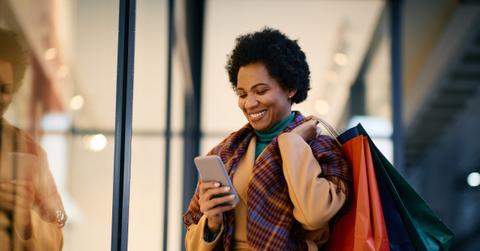 Happy black woman texting on cell phone while shopping in city.
