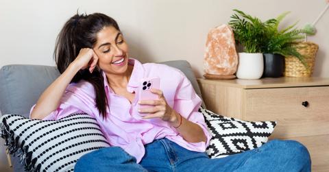 Beautiful young happy woman with pink skirt sitting at home and using mobile phone