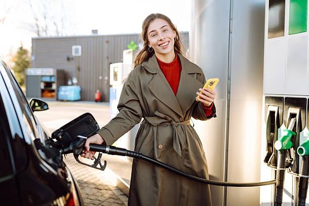 ///imgi__young woman holding phone in hand filling her car at gas station