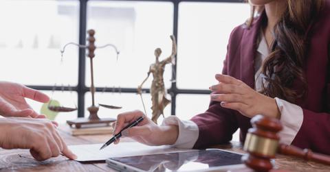 Lawyer guiding client on where to sign a legal document, with scales of justice and a Themis statue prominently displayed in the background, creating a professional atmosphere