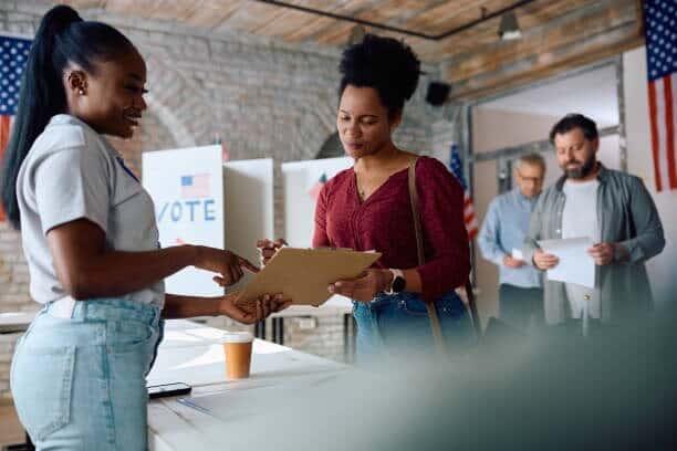 ///imgi__polling place volunteer assisting black woman to sign up for voting during usa elections