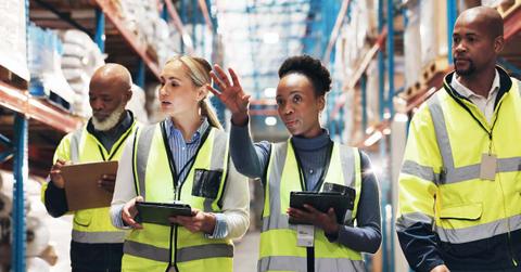 Warehouse, supply chain and people with tablet in discussion for inspection checklist, export or plan. Dropshipping, meeting and work with tech by shelf for inventory, update or operations management
