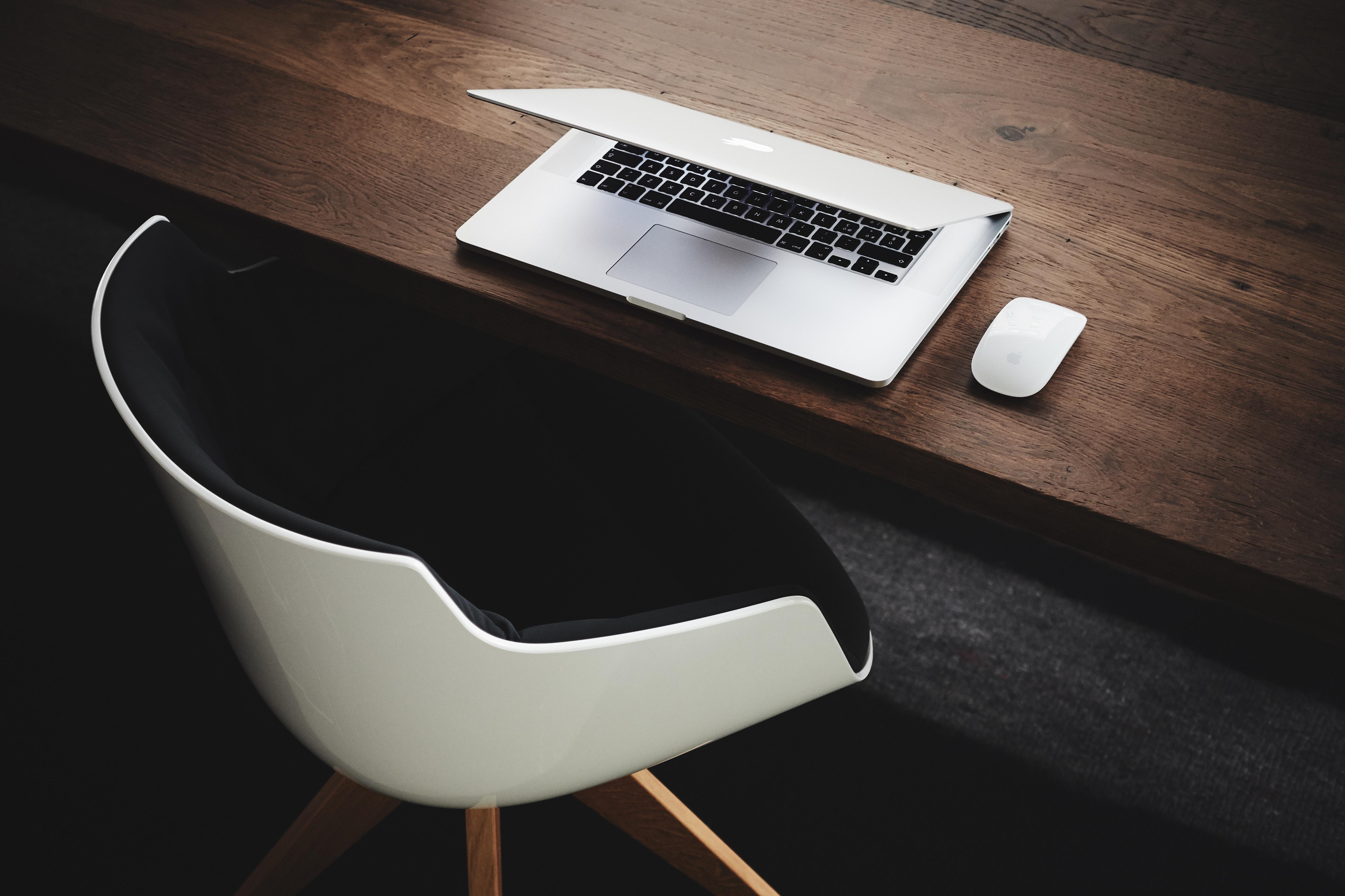 An empty chair sits are a wooden desk with a laptop partially shut.